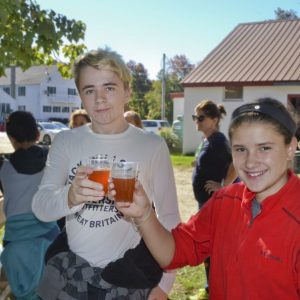 Two people clinking their cups of cider in front of the barn at East Hill Farm School
